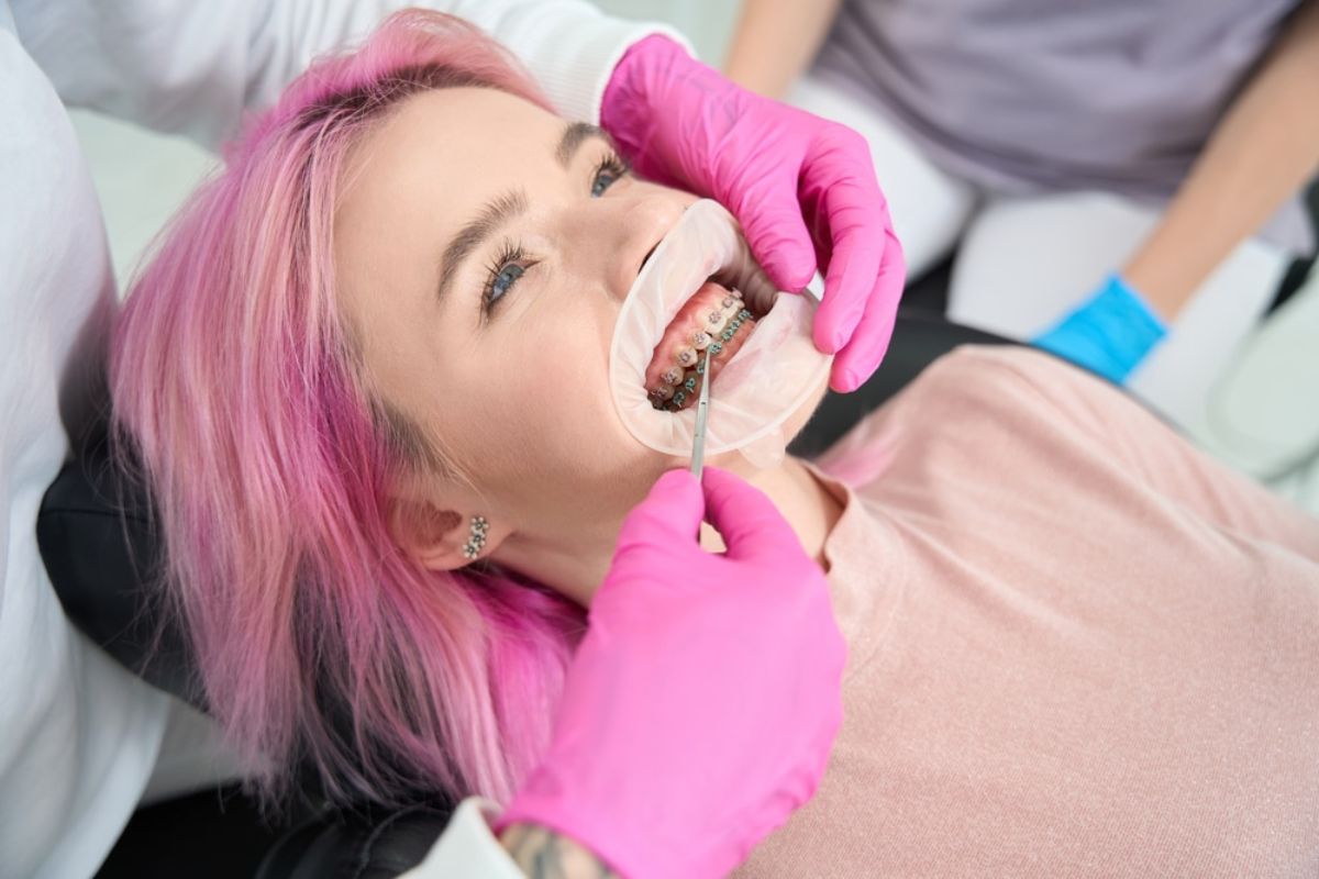 Patient receiving dental examination in bright clinical setting with pink protective covering.