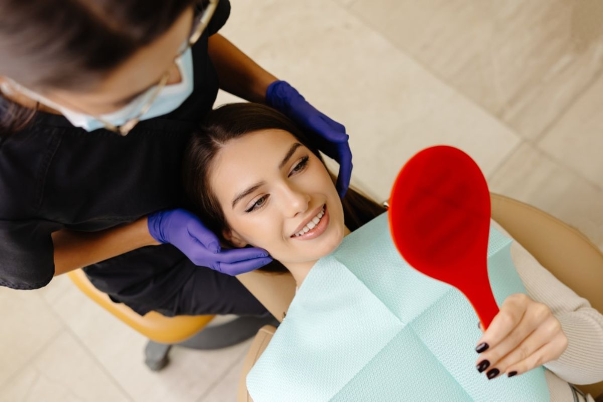 Dental patient smiling while holding red heart-shaped object during examination with dentist in office.