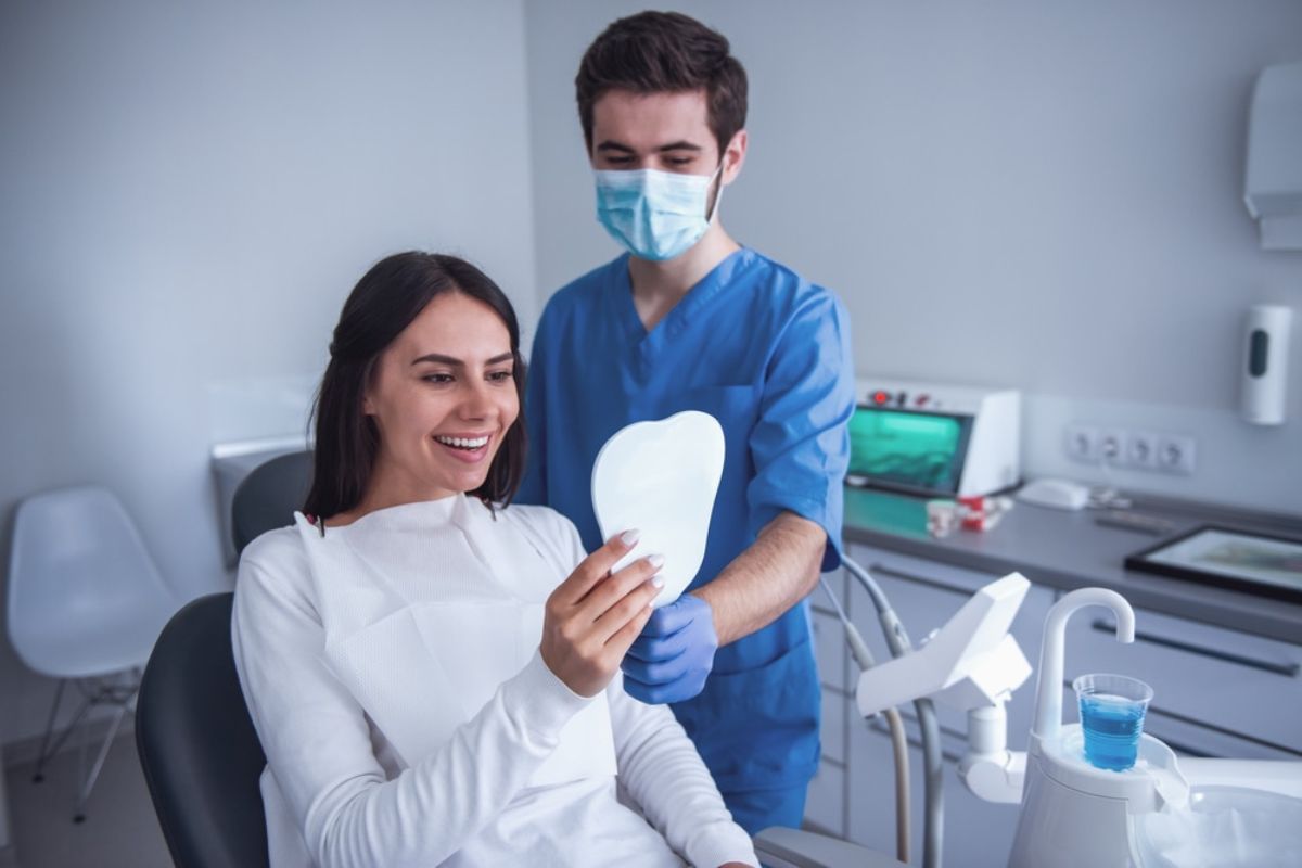 Dentist in blue scrubs and mask showing dental model to patient in dental office.