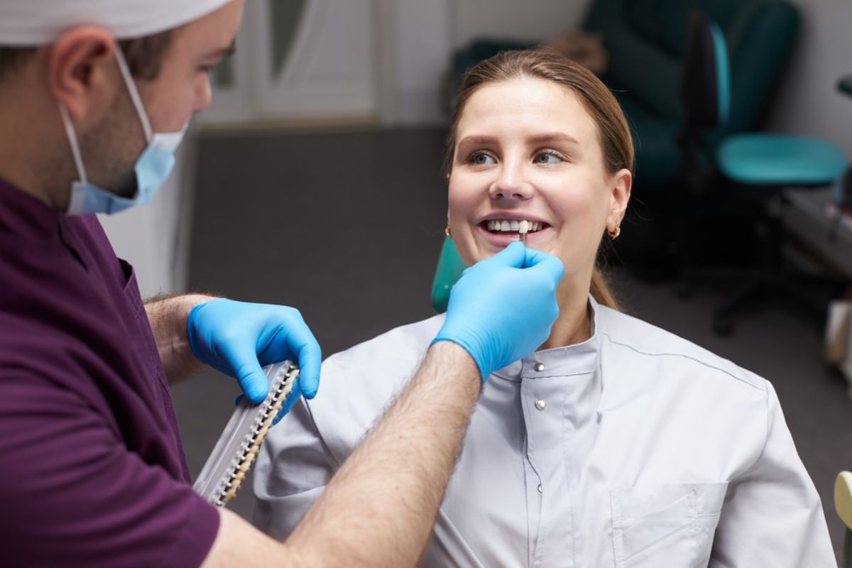 Dentist in blue gloves examining male patient's throat in clinical dental office setting.