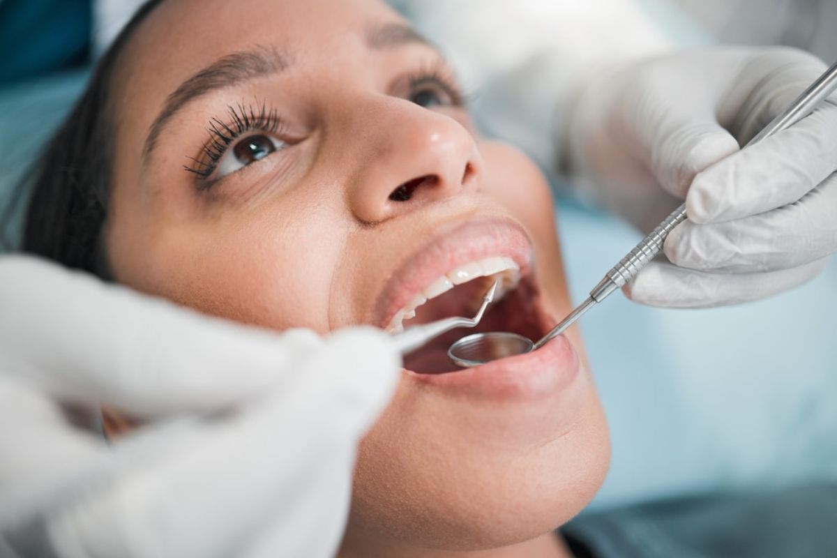 Patient receiving dental examination in dental office with dentist using mirror and tools.