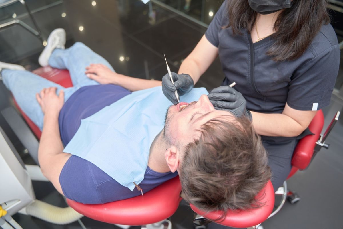 Dentist examining patient's teeth in dental chair during oral examination.