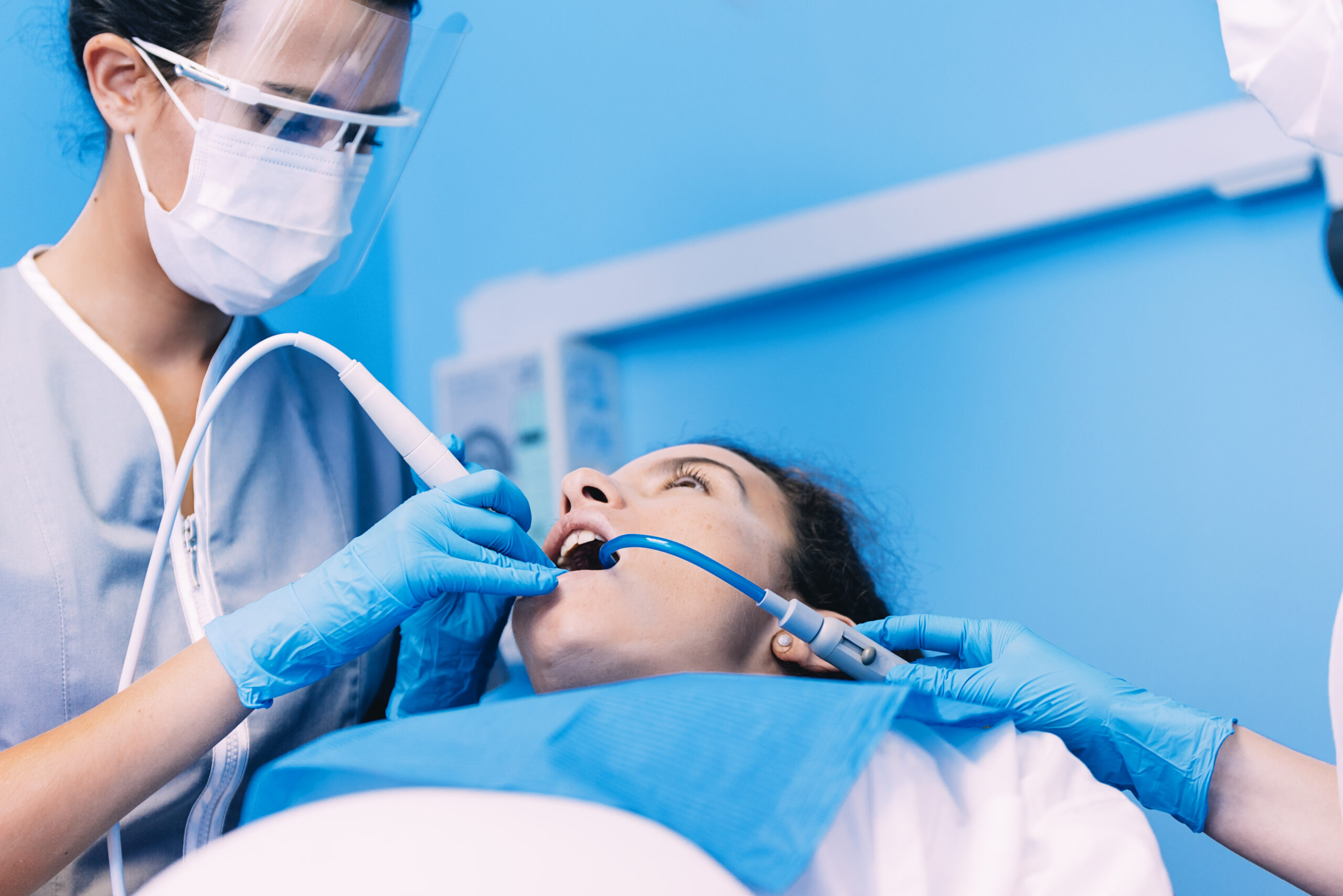 Dentist examining patient's teeth in bright blue clinical treatment room