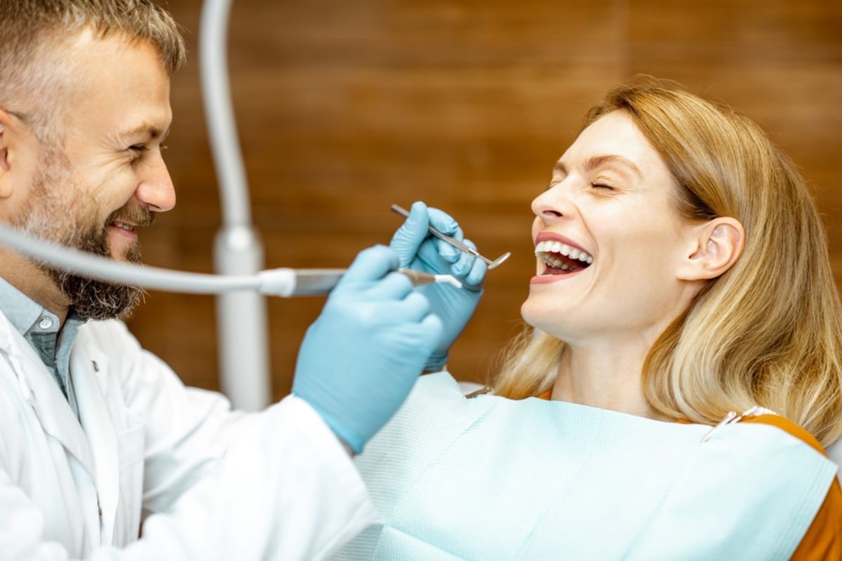 Dentist in blue gloves examining smiling patient's teeth in dental office.